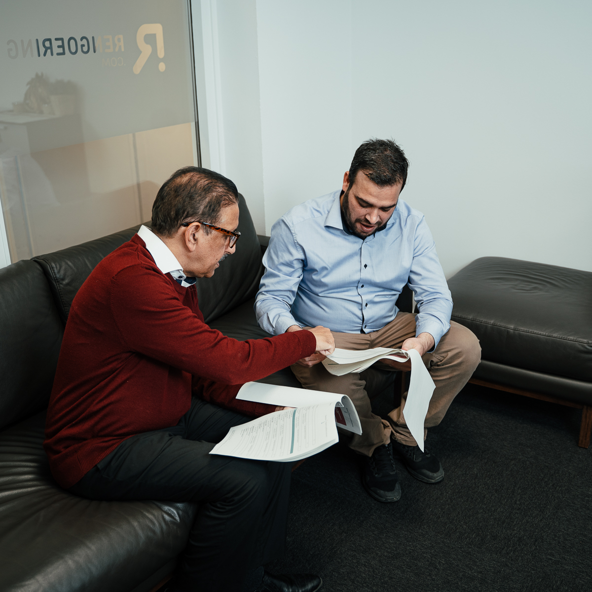 Two advisors reviewing printed tender documents together in a Danish office